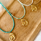 Collier pierres fines vert d’eau et coquillage doré porté autour du cou