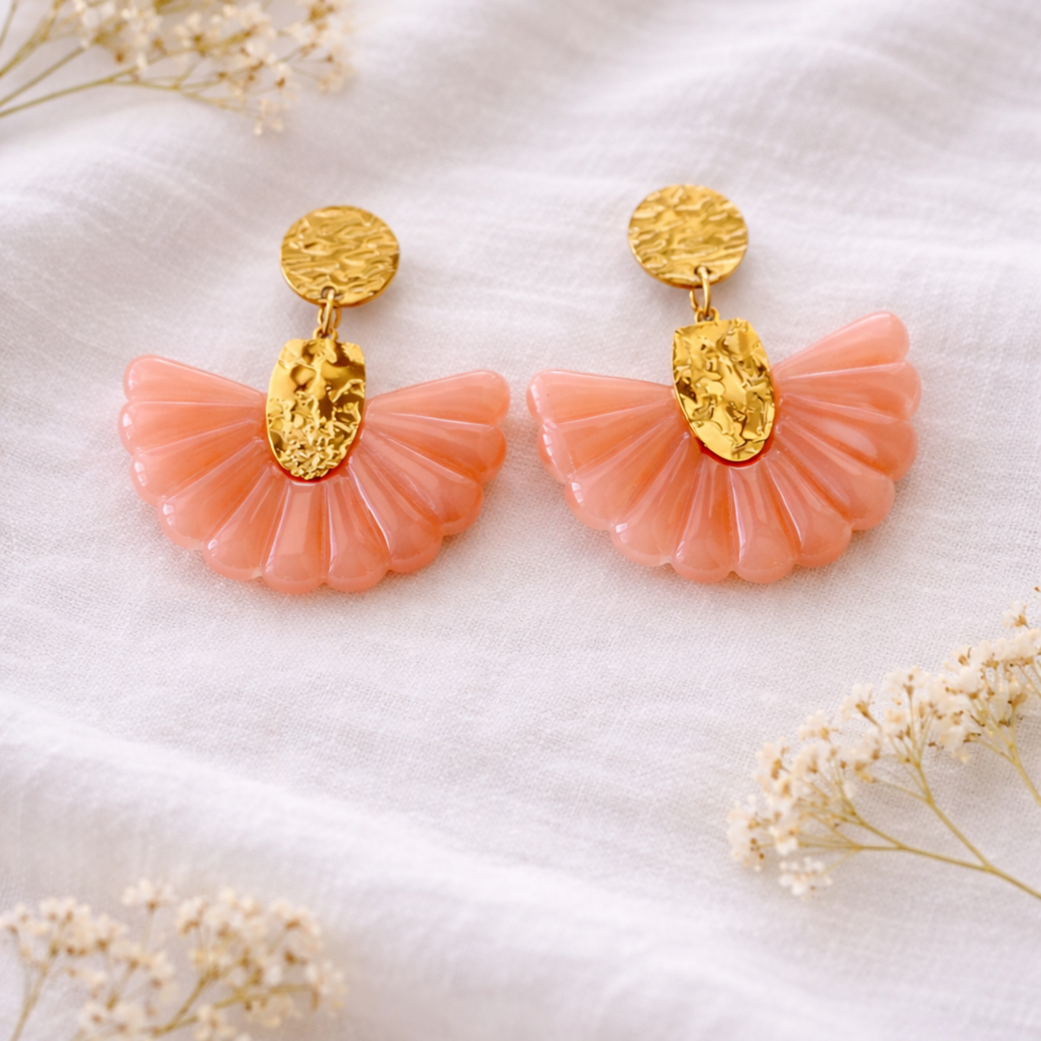 Boucles d'oreilles bohème portées de profil — pendentif éventail en résine nacrée blanche fixé sur une pièce en acier inoxydable doré à l'effet martelé, sur fond de chemise blanche