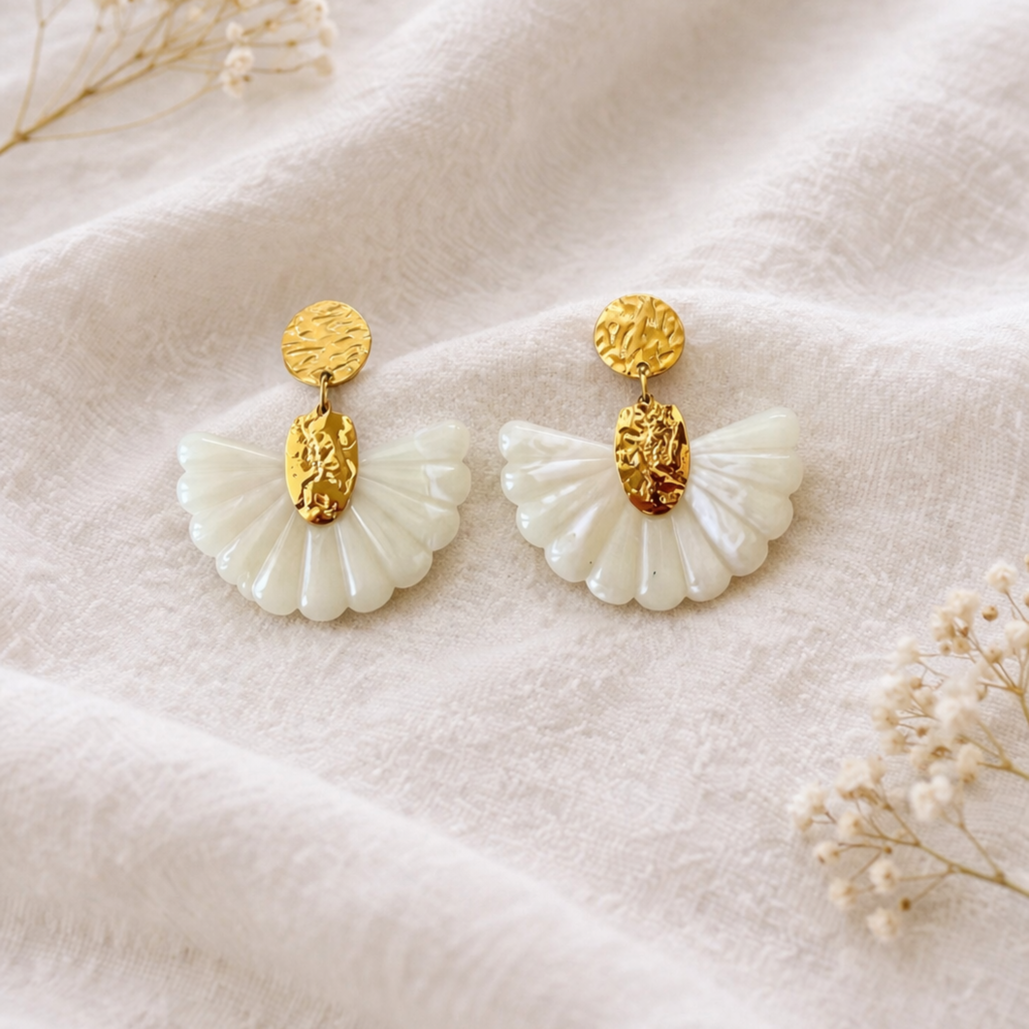 Boucles d'oreilles bohème portées de profil — pendentif éventail en résine nacrée blanche fixé sur une pièce en acier inoxydable doré à l'effet martelé, sur fond de chemise blanche