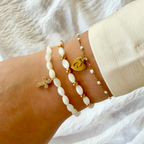 Bracelet femme en perles de nacre blanches avec pendentif croix dorée porté au poignet