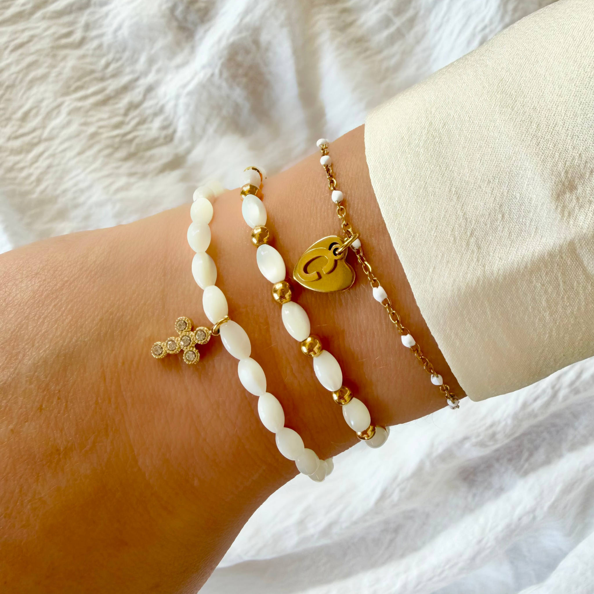 Bracelet femme en perles de nacre blanches avec pendentif croix dorée porté au poignet