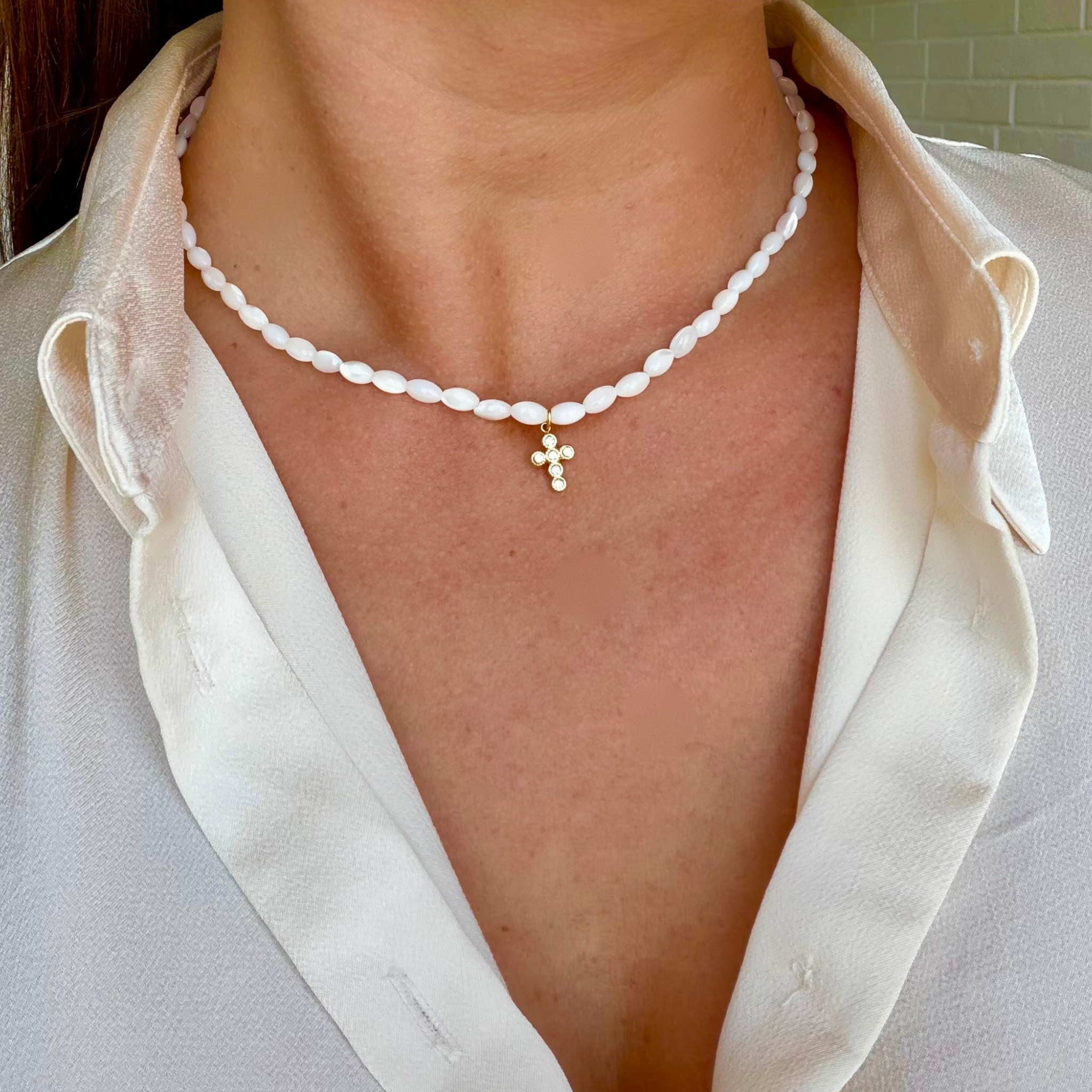 Collier femme en perles de nacre blanches avec pendentif croix dorée en acier inoxydable porté autour du cou